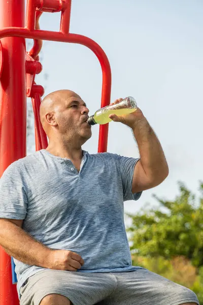 A man drinks isotonic sports drink sitting at the machine in the biohealth park
