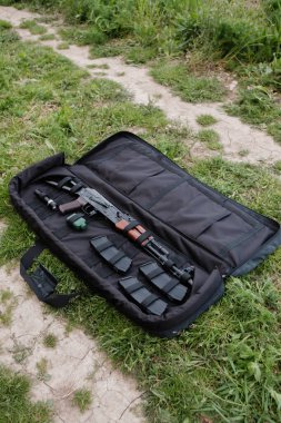 Üzerinde AK-47, şarjör ve fener bulunan üstü açık bir silah çantası.