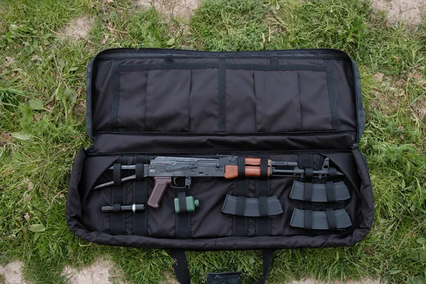 Uncovered gun case with AK-47, magazines, and flashlight lying on the ground black