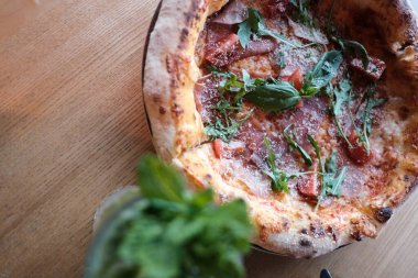 Domatesli, peynirli ve ahşap masadaki Arugula peynirli lezzetli Prosciutto Pizza.