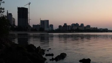 Gün batımında sakin, güzel nehir Dinyeper 'ı. Dinyeper şehrinin sol yakasının manzarası. Şehir turuncu gün batımı ışıklarıyla. Gerçek zamanlı UHD 4K videosu. Ukrayna şehrinin akşam manzarası