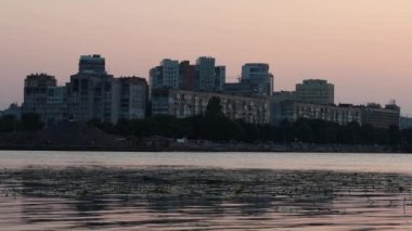 Gün batımında sakin, güzel nehir Dinyeper 'ı. Dinyeper şehrinin sol yakasının manzarası. Şehir turuncu gün batımı ışıklarıyla. Gerçek zamanlı UHD 4K videosu. Ukrayna şehrinin akşam manzarası