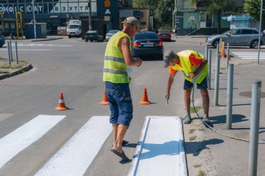 İşçiler yaya geçidine beyaz çizgiler çiziyor. Yol işçileri yol yüzeyine beyaz bir çizgi çekiyor. Hareket çizgisini boyuyorum. DNIPRO, UKRAINE - 16 Ağustos 2023