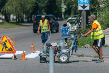İşçiler yaya geçidine beyaz çizgiler çiziyor. Yol işçileri yol yüzeyine beyaz bir çizgi çekiyor. Hareket çizgisini boyuyorum. DNIPRO, UKRAINE - 16 Ağustos 2023
