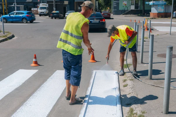 İşçiler yaya geçidine beyaz çizgiler çiziyor. Yol işçileri yol yüzeyine beyaz bir çizgi çekiyor. Hareket çizgisini boyuyorum. DNIPRO, UKRAINE - 16 Ağustos 2023