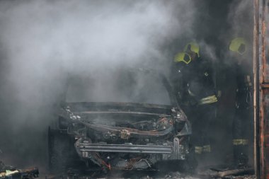 İtfaiyeciler yanan bir arabayı garajda söndürür. Yanmış araba. Kurtarıcılar. Sağlam duman. Acil durum. Sigorta davası.
