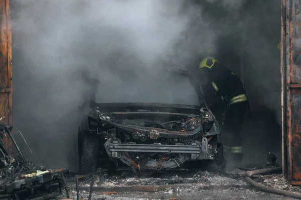 İtfaiyeciler yanan bir arabayı garajda söndürür. Yanmış araba. Kurtarıcılar. Sağlam duman. Acil durum. Sigorta davası.