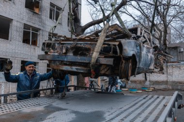 Arabayı bir çekiciye yüklüyorlar. Shahed evleri havaya uçurdu. Saldırıdan sonra bombalanmış bir bina ve yanmış arabalar. Ukrayna 'da savaş, Dnipro şehri. Yanmış araba..