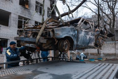 Arabayı bir çekiciye yüklüyorlar. Shahed evleri havaya uçurdu. Saldırıdan sonra bombalanmış bir bina ve yanmış arabalar. Ukrayna 'da savaş, Dnipro şehri. Yanmış araba..