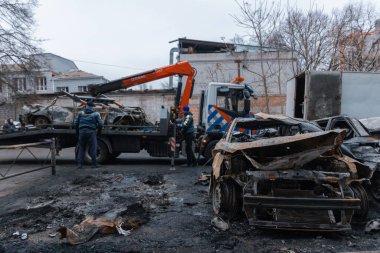 Arabayı bir çekiciye yüklüyorlar. Shahed evleri havaya uçurdu. Saldırıdan sonra bombalanmış bir bina ve yanmış arabalar. Ukrayna 'da savaş, Dnipro şehri. Yanmış araba..