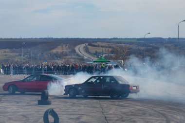 Bir yarış arabası hızlı bir şekilde sürüklenir. Sürücü arabayı sürüklüyor. Arka planda dumanla savrulan bir araba, dumanlı tekerlekler. Hız. Ekstrem spor. Rotadan. DNIPRO, UKRAINE - 30 Mart 2024.