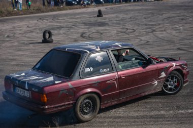Bir yarış arabası hızlı bir şekilde sürüklenir. Sürücü arabayı sürüklüyor. Arka planda dumanla savrulan bir araba, dumanlı tekerlekler. Hız. Ekstrem spor. Rotadan. DNIPRO, UKRAINE - 30 Mart 2024.