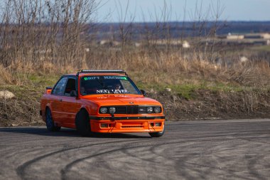 Bir yarış arabası hızlı bir şekilde sürüklenir. Sürücü arabayı sürüklüyor. Arka planda dumanla savrulan bir araba, dumanlı tekerlekler. Hız. Ekstrem spor. Rotadan. DNIPRO, UKRAINE - 30 Mart 2024.