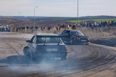 Bir yarış arabası hızlı bir şekilde sürüklenir. Sürücü arabayı sürüklüyor. Arka planda dumanla savrulan bir araba, dumanlı tekerlekler. Hız. Ekstrem spor. Rotadan. DNIPRO, UKRAINE - 30 Mart 2024.