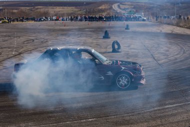 Bir yarış arabası hızlı bir şekilde sürüklenir. Sürücü arabayı sürüklüyor. Arka planda dumanla savrulan bir araba, dumanlı tekerlekler. Hız. Ekstrem spor. Rotadan. DNIPRO, UKRAINE - 30 Mart 2024.