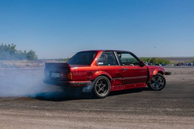Bir yarış arabası hızlı bir şekilde sürüklenir. Sürücü arabayı sürüklüyor. Arka planda dumanla savrulan bir araba, dumanlı tekerlekler. Hız. Ekstrem spor. Rotadan. DNIPRO, UKRAINE - 25 Mayıs 2024