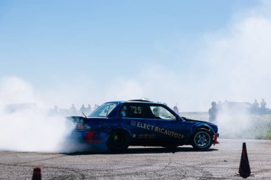 Bir yarış arabası hızlı bir şekilde sürüklenir. Sürücü arabayı sürüklüyor. Arka planda dumanla savrulan bir araba, dumanlı tekerlekler. Hız. Ekstrem spor. Rotadan. DNIPRO, UKRAINE - 25 Mayıs 2024