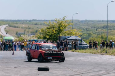 Bir yarış arabası hızlı bir şekilde sürüklenir. Sürücü arabayı sürüklüyor. Arka planda dumanla savrulan bir araba, dumanlı tekerlekler. Hız. Ekstrem spor. Rotadan. DNIPRO, UKRAINE - 25 Mayıs 2024