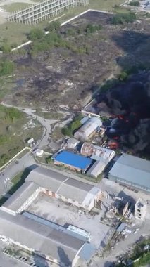 Büyük bir yangın deposunun insansız hava aracı videosu. Gökyüzünde yoğun siyah duman. Fabrika yanıyor. Depo endüstriyel hangarı. Kurtarma ekipleri yangını söndürüyor. Yukarıdan bak. Dikey video.