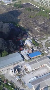 Büyük bir yangın deposunun insansız hava aracı videosu. Gökyüzünde yoğun siyah duman. Fabrika yanıyor. Depo endüstriyel hangarı. Kurtarma ekipleri yangını söndürüyor. Yukarıdan bak. Dikey video.
