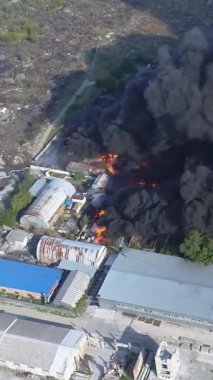 Büyük bir yangın deposunun insansız hava aracı videosu. Gökyüzünde yoğun siyah duman. Fabrika yanıyor. Depo endüstriyel hangarı. Kurtarma ekipleri yangını söndürüyor. Yukarıdan bak. Dikey video.