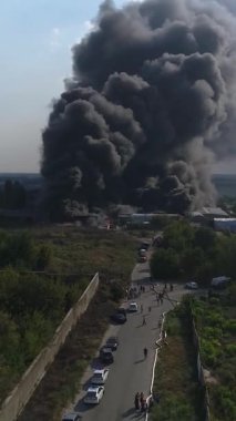 Büyük bir yangın deposunun insansız hava aracı videosu. Gökyüzünde yoğun siyah duman. Fabrika yanıyor. Depo endüstriyel hangarı. Kurtarma ekipleri yangını söndürüyor. Yukarıdan bak. Dikey video.