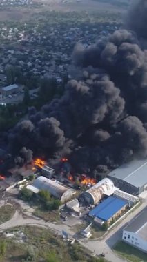 Büyük bir yangın deposunun insansız hava aracı videosu. Gökyüzünde yoğun siyah duman. Fabrika yanıyor. Depo endüstriyel hangarı. Kurtarma ekipleri yangını söndürüyor. Yukarıdan bak. Dikey video.
