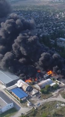 Büyük bir yangın deposunun insansız hava aracı videosu. Gökyüzünde yoğun siyah duman. Fabrika yanıyor. Depo endüstriyel hangarı. Kurtarma ekipleri yangını söndürüyor. Yukarıdan bak. Dikey video.
