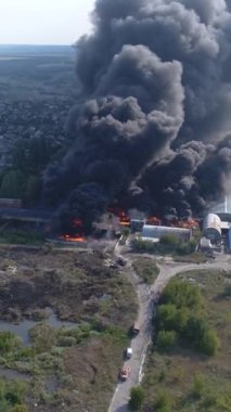 Büyük bir yangın deposunun insansız hava aracı videosu. Gökyüzünde yoğun siyah duman. Fabrika yanıyor. Depo endüstriyel hangarı. Kurtarma ekipleri yangını söndürüyor. Yukarıdan bak. Dikey video.