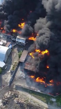Büyük bir yangın deposunun insansız hava aracı videosu. Gökyüzünde yoğun siyah duman. Fabrika yanıyor. Depo endüstriyel hangarı. Kurtarma ekipleri yangını söndürüyor. Yukarıdan bak. Dikey video.
