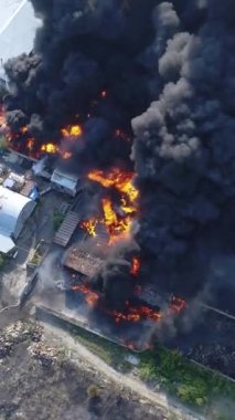Büyük bir yangın deposunun insansız hava aracı videosu. Gökyüzünde yoğun siyah duman. Fabrika yanıyor. Depo endüstriyel hangarı. Kurtarma ekipleri yangını söndürüyor. Yukarıdan bak. Dikey video.