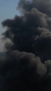 Büyük bir yangın deposunun insansız hava aracı videosu. Gökyüzünde yoğun siyah duman. Fabrika yanıyor. Depo endüstriyel hangarı. Kurtarma ekipleri yangını söndürüyor. Yukarıdan bak. Dikey video.