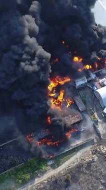 Büyük bir yangın deposunun insansız hava aracı videosu. Gökyüzünde yoğun siyah duman. Fabrika yanıyor. Depo endüstriyel hangarı. Kurtarma ekipleri yangını söndürüyor. Yukarıdan bak. Dikey video.