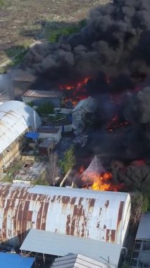 Büyük bir yangın deposunun insansız hava aracı videosu. Gökyüzünde yoğun siyah duman. Fabrika yanıyor. Depo endüstriyel hangarı. Kurtarma ekipleri yangını söndürüyor. Yukarıdan bak. Dikey video.