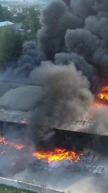 Büyük bir yangın deposunun insansız hava aracı videosu. Gökyüzünde yoğun siyah duman. Fabrika yanıyor. Depo endüstriyel hangarı. Kurtarma ekipleri yangını söndürüyor. Yukarıdan bak. Dikey video.