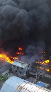 Büyük bir yangın deposunun insansız hava aracı videosu. Gökyüzünde yoğun siyah duman. Fabrika yanıyor. Depo endüstriyel hangarı. Kurtarma ekipleri yangını söndürüyor. Yukarıdan bak. Dikey video.