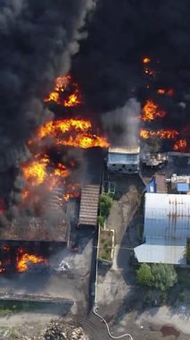 Büyük bir yangın deposunun insansız hava aracı videosu. Gökyüzünde yoğun siyah duman. Fabrika yanıyor. Depo endüstriyel hangarı. Kurtarma ekipleri yangını söndürüyor. Yukarıdan bak. Dikey video.