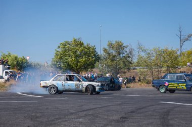 Bir yarış arabası hızlı bir şekilde sürüklenir. Sürücü arabayı sürüklüyor. Arka planda dumanla savrulan bir araba, dumanlı tekerlekler. Hız. Ekstrem spor. Yönlendirme. 
