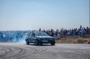 Bir yarış arabası hızlı bir şekilde sürüklenir. Sürücü arabayı sürüklüyor. Arka planda dumanla savrulan bir araba, dumanlı tekerlekler. Hız. Ekstrem spor. Yönlendirme. 