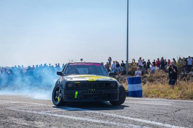 Bir yarış arabası hızlı bir şekilde sürüklenir. Sürücü arabayı sürüklüyor. Arka planda dumanla savrulan bir araba, dumanlı tekerlekler. Hız. Ekstrem spor. Yönlendirme. 