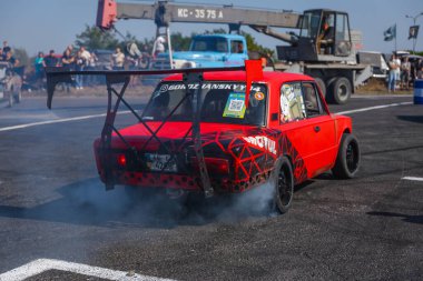Bir yarış arabası hızlı bir şekilde sürüklenir. Sürücü arabayı sürüklüyor. Arka planda dumanla savrulan bir araba, dumanlı tekerlekler. Hız. Ekstrem spor. Yönlendirme. 