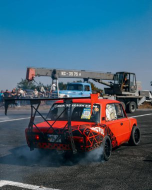 Bir yarış arabası hızlı bir şekilde sürüklenir. Sürücü arabayı sürüklüyor. Arka planda dumanla savrulan bir araba, dumanlı tekerlekler. Hız. Ekstrem spor. Yönlendirme. 