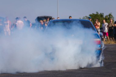 Bir yarış arabası hızlı bir şekilde sürüklenir. Sürücü arabayı sürüklüyor. Arka planda dumanla savrulan bir araba, dumanlı tekerlekler. Hız. Ekstrem spor. Yönlendirme. 