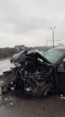Islak bir yolda kaza yaptıktan sonra kaza yapmış siyah bir araba. Ön tarafı parçalanmış ve kaputu açık bir araba şehir caddesinde. Yağmurlu bir hava. İki araba arasındaki çarpışmadan sonra...