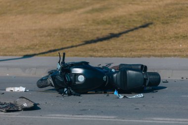 Asfaltta ciddi hasar görmüş siyah bir motosiklet var. Kazaya yakın çekim. Kontrolü kaybettim ve düştüm. Araba sürme tehlikesi. Başka bir araca çarpmış. Kırık farlar ve eğilmiş gidonlar..