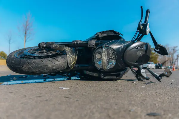 Asfaltta ciddi hasar görmüş siyah bir motosiklet var. Kazaya yakın çekim. Kontrolü kaybettim ve düştüm. Araba sürme tehlikesi. Başka bir araca çarpmış. Kırık farlar ve eğilmiş gidonlar..