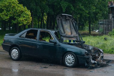 Kaputu açık, yanmış bir arabanın yakın çekimi. Hasarlı motor bölümünün parçaları, erimiş parçalar ve yanmış kablolar görülebilir durumda. Kurum ve kül izleri görülüyor ve yangın izleri de görülüyor..