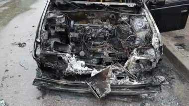 Kaputu açık, yanmış bir arabanın yakın çekimi. Hasarlı motor bölümünün parçaları, erimiş parçalar ve yanmış kablolar görülebilir durumda. Kurum ve kül izleri görülüyor ve yangın izleri de görülüyor..