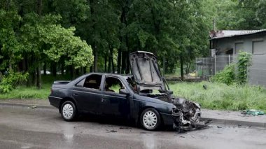 Kaputu açık, yanmış bir arabanın yakın çekimi. Hasarlı motor bölümünün parçaları, erimiş parçalar ve yanmış kablolar görülebilir durumda. Kurum ve kül izleri görülüyor ve yangın izleri de görülüyor..