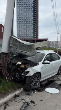 Şehir yolundaki bir kazadan sonra ağır hasar görmüş beyaz bir sedan. Araba bir direğe çarptı, ön kısmı parçalandı, kaput açık. Kaza, yol tehlikesi ve sigorta kavramı.